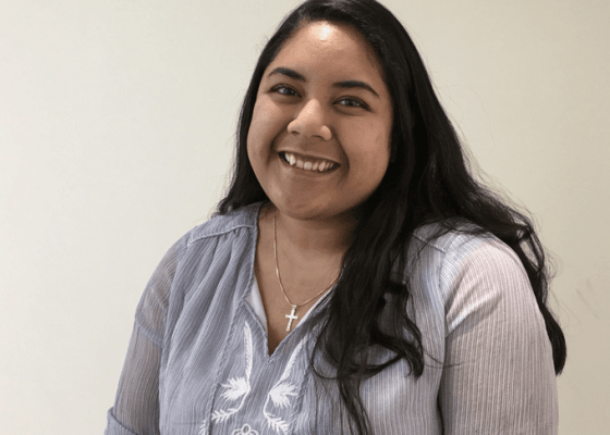 Close-up of Welly smiling, black hair down, wearing necklace with a cross.