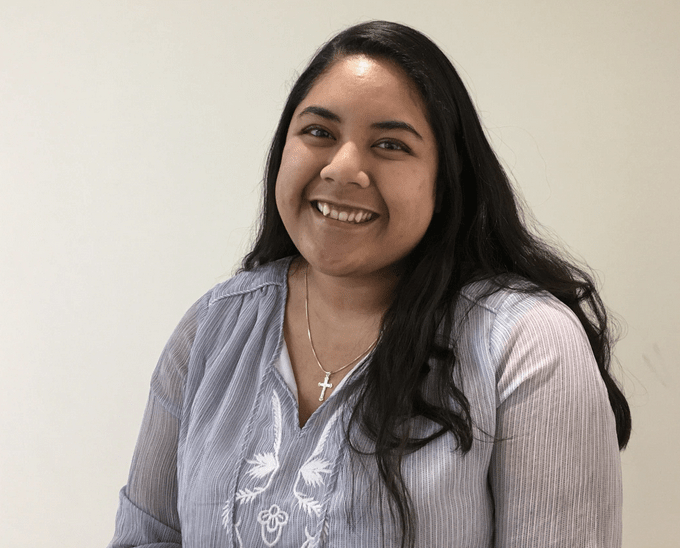Close-up of Welly smiling, black hair down, wearing necklace with a cross.