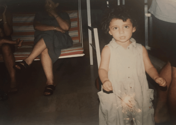 Little child holding sparkle in evening light, swing with women sitting down in the background