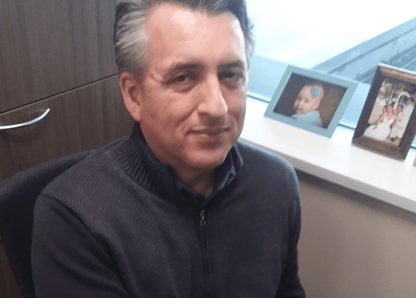 Man sits on chair in office setting, smiling.