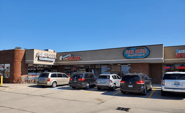 Store fronts in strip mall, many have text in Arabic in signs.