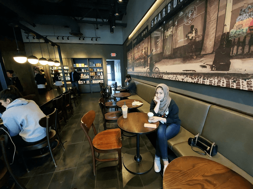 Woman sits in coffee shop; a few other people at tables.