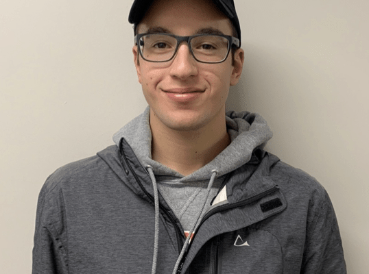 Young man with Oakland University baseball cap smiles.