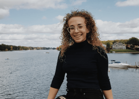 Young woman smiling, posing with lake behind.