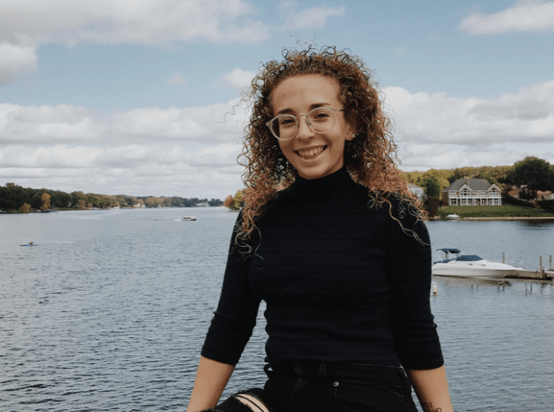 Young woman smiling, posing with lake behind.