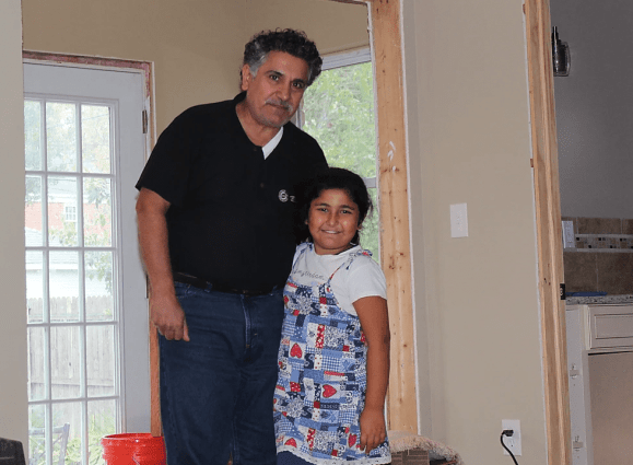 Man and little girl smile in doorway of home that looks under construction.