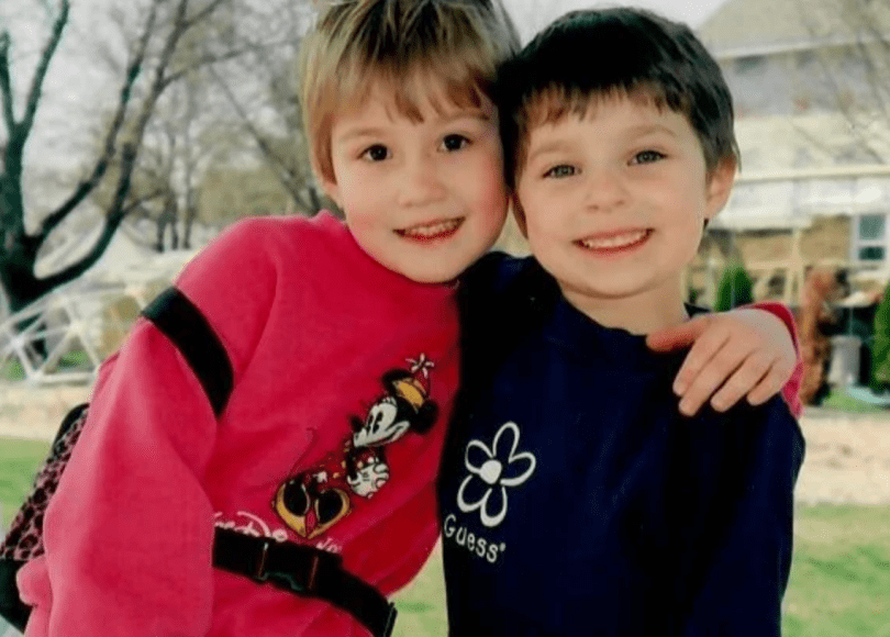 Two young children smile and hug each other.