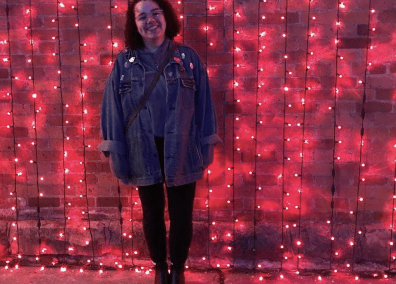 Young woman smiles by wall covered in red lights.