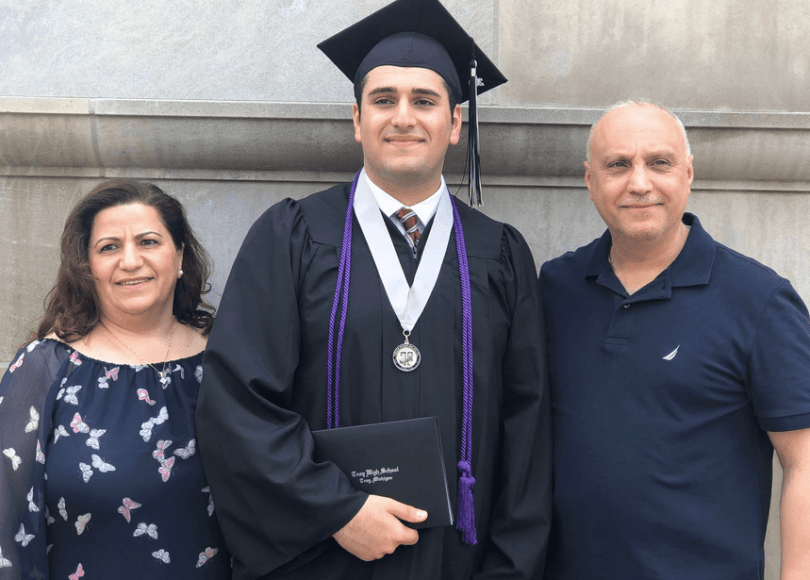 Man in cap-and-gown attire poses with smiling parents.