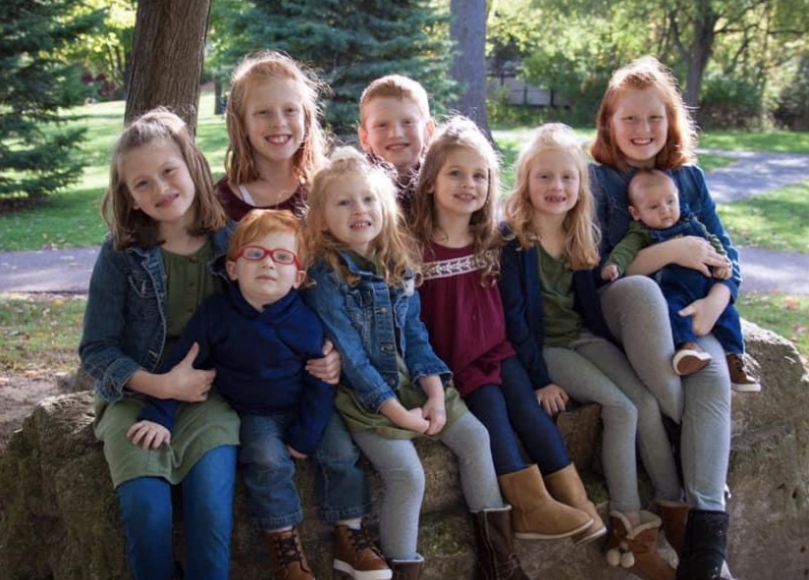 Nine children smile huddled together on a large rock.