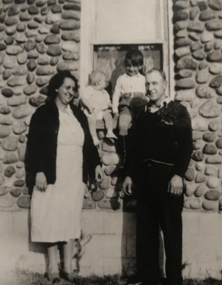 Black and white photo of smiling adults, two small children between them sitting higher up on a window sill.