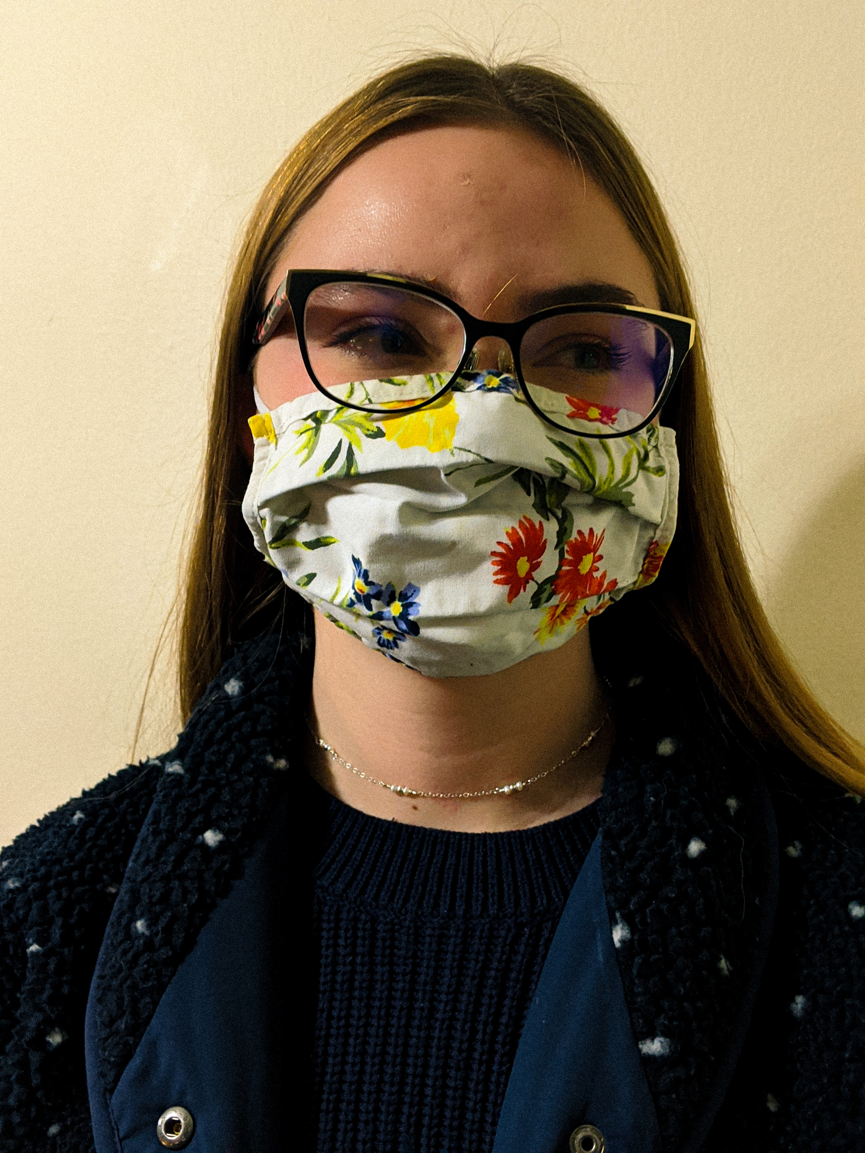 Close-up of white young woman with long hair and glasses, wearing a flowery face mask.