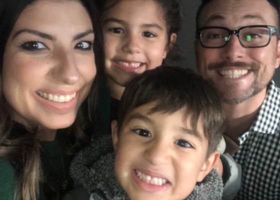 Family of four smiling into camera, only heads visible, two parents, a young girl and a young boy