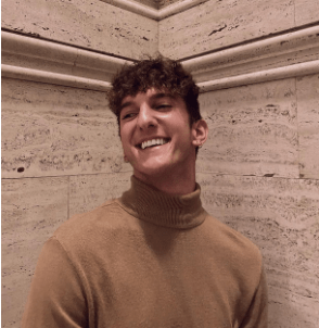 Young man laughs looking sideways, marble wall behind him