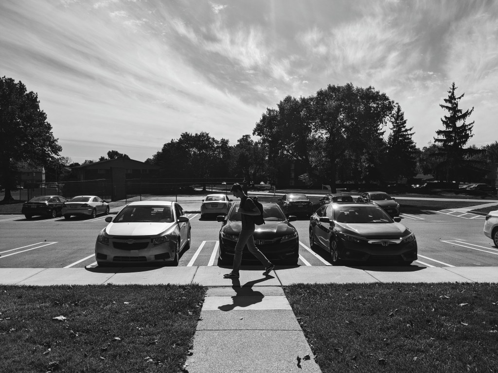 Black and white picture of young man walking with backpack in parking lot
