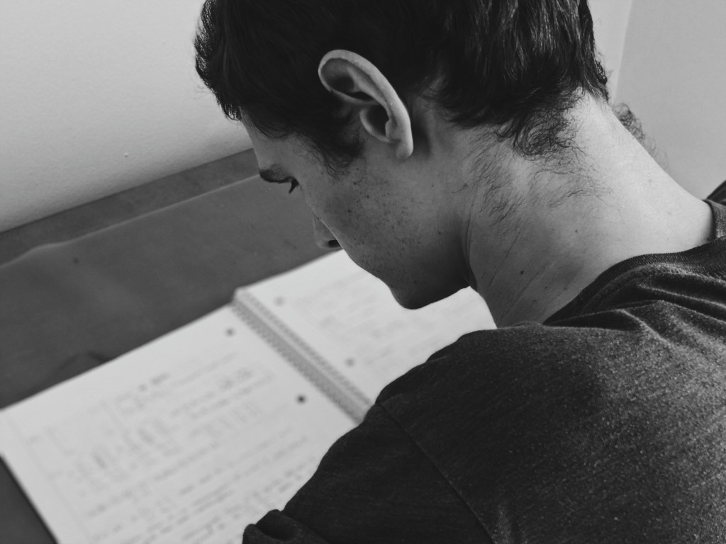 Black and white young man sits at desk reading notebook